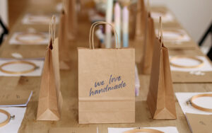 Kreativ-Workshop Set-Up von we love handmade in Wien: Holztisch mit Stickrahmen, Workbooks und Papiertüten mit Logo für DIY-Teilnehmer:innen.