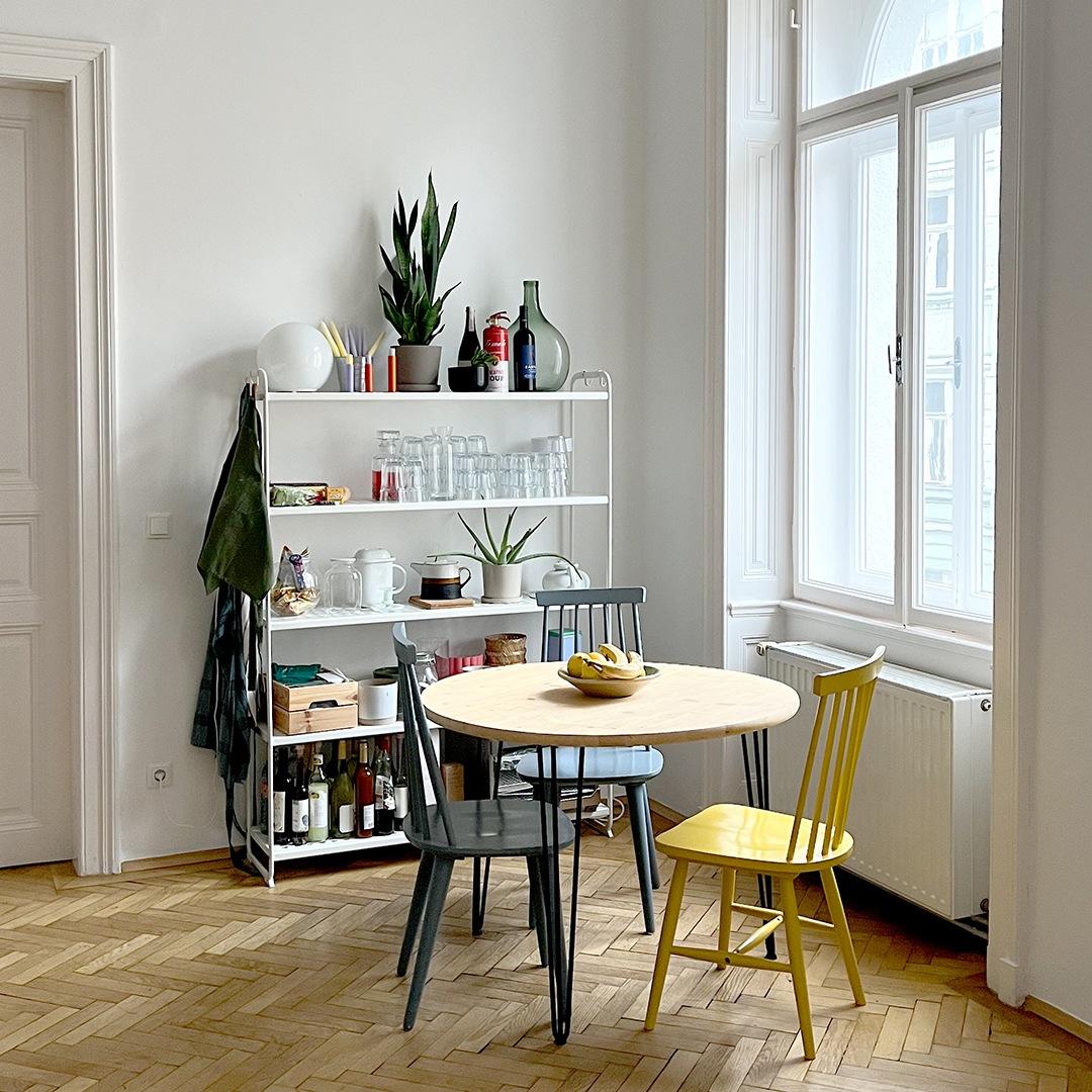 Helles Atelier in Wien mit rundem Tisch, bunten Stühlen und Regal mit Gläsern – Workshoplocation für kreative Events und Junggesellinnenabschiede.