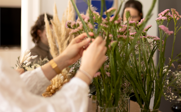 Teilnehmerin arrangiert zarte rosa Trockenblumen bei einem DIY-Workshop in Wien für das Binden von Blumenkränzen.
