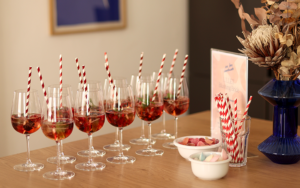 Eine Reihe gefüllter Aperitivo-Gläser mit Beeren und rot-weiß gestreiften Strohhalmen auf einem Holztisch im we love handmade Studio in Wien Neubau. | we love handmade