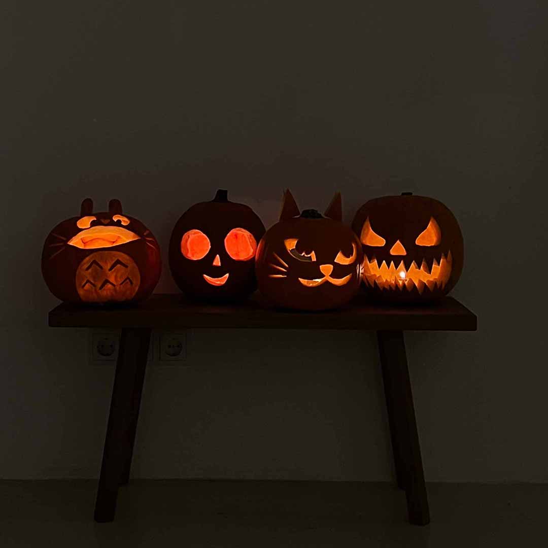Vier selbstgeschnitzte, stimmungsvoll erleuchtete Halloween-Kürbisse auf einer Holzbank bei der we love handmade Craft & Aperitivo Night in Wien.