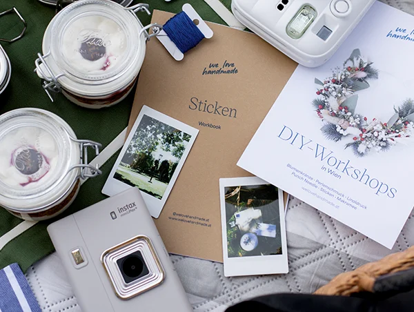 DIY-Workshops-Flyer von we love handmade neben Stick-Workbook, Stickgarn und Instax Kamera auf einer Picknickdecke