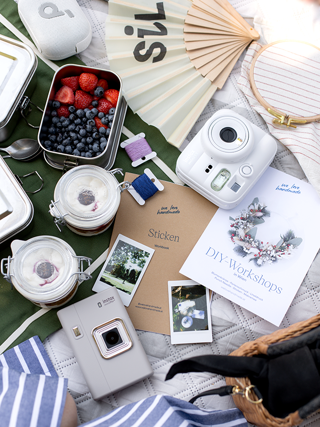 Picknick-Flatlay mit Beeren, Trifle im Glas, Instax Kamera, Sofortbildfotos, Stickgarnen und einem Flyer für DIY-Workshops von we love handmade