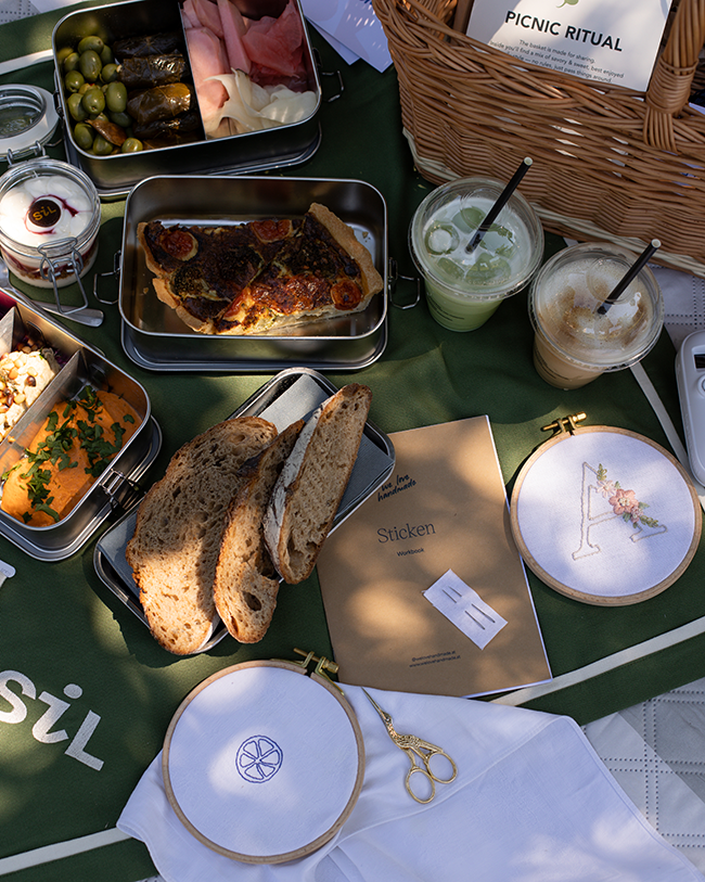 Picknick auf grünem SiL Tischtuch mit Oliven, gefüllten Weinblättern, Quiche, Dips, Brot, Getränken und einem Stickrahmen