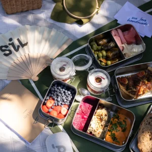 SiL Picknickkorb Inhalt mit Oliven, Weinblättern, Joghurt und Quiche neben Stickutensilien