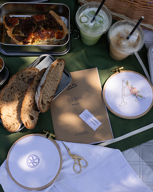 Picknick-Flatlay mit Quiche, Brot, Eiskaffee, we love handmade Stick-Workbook und zwei Stickrahmen mit Monogramm und Zitronenmotiv