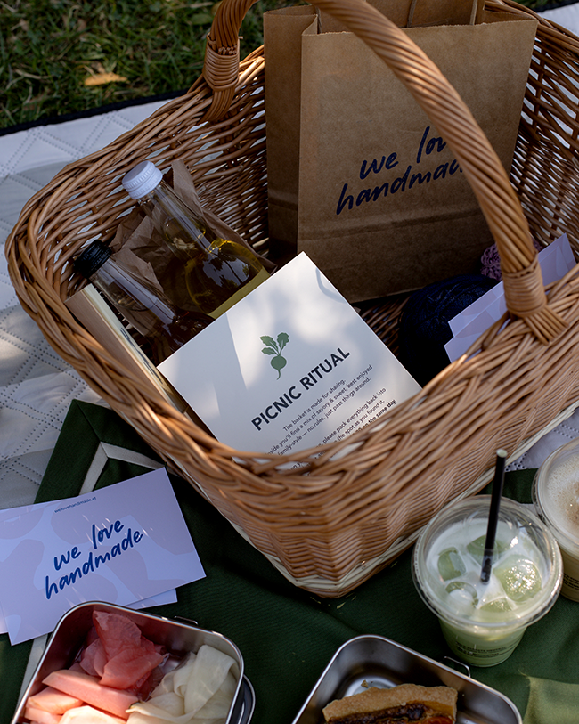 Weidenkorb mit Picnic Ritual Karte, Papiertasche und Visitenkarten von we love handmade sowie Getränken auf einer Picknickdecke