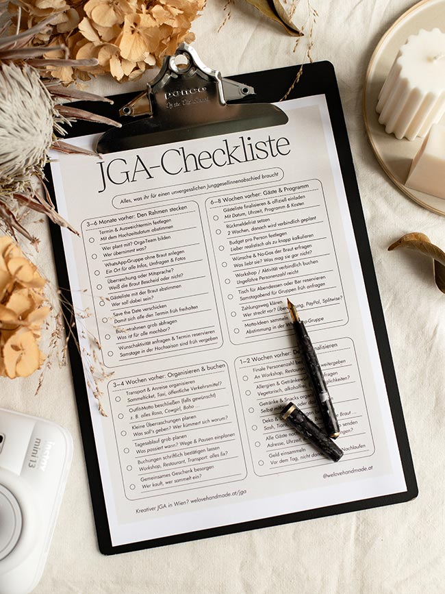 Ausgedruckte JGA-Checkliste auf einem schwarzen Penco-Klemmbrett neben einer Sofortbildkamera und Trockenblumen.