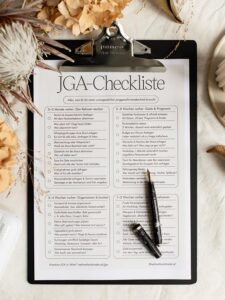 Draufsicht auf die ausgedruckte JGA-Checkliste auf einem schwarzen Clipboard mit zwei schwarzen Füllfederhaltern darauf.