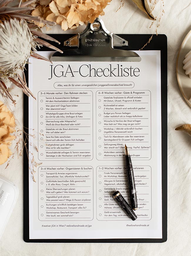 Draufsicht auf die ausgedruckte JGA-Checkliste auf einem schwarzen Clipboard mit zwei schwarzen Füllfederhaltern darauf.