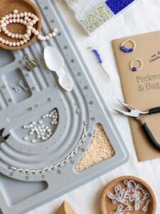 Graues Perlensortierbrett mit Süßwasserperlen, Perlen-Zubehör, Brillenketten-Schlaufen und dem gedruckten we love handmade Workbook für den Perlenschmuck & Bag-Charms Workshop.