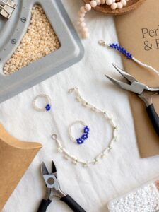 Flachbild-Aufnahme von DIY Perlenschmuck, Ringen mit Blumenmuster, Perlen-Tablett und Schmuckwerkzeug beim we love handmade Workshop in Wien.