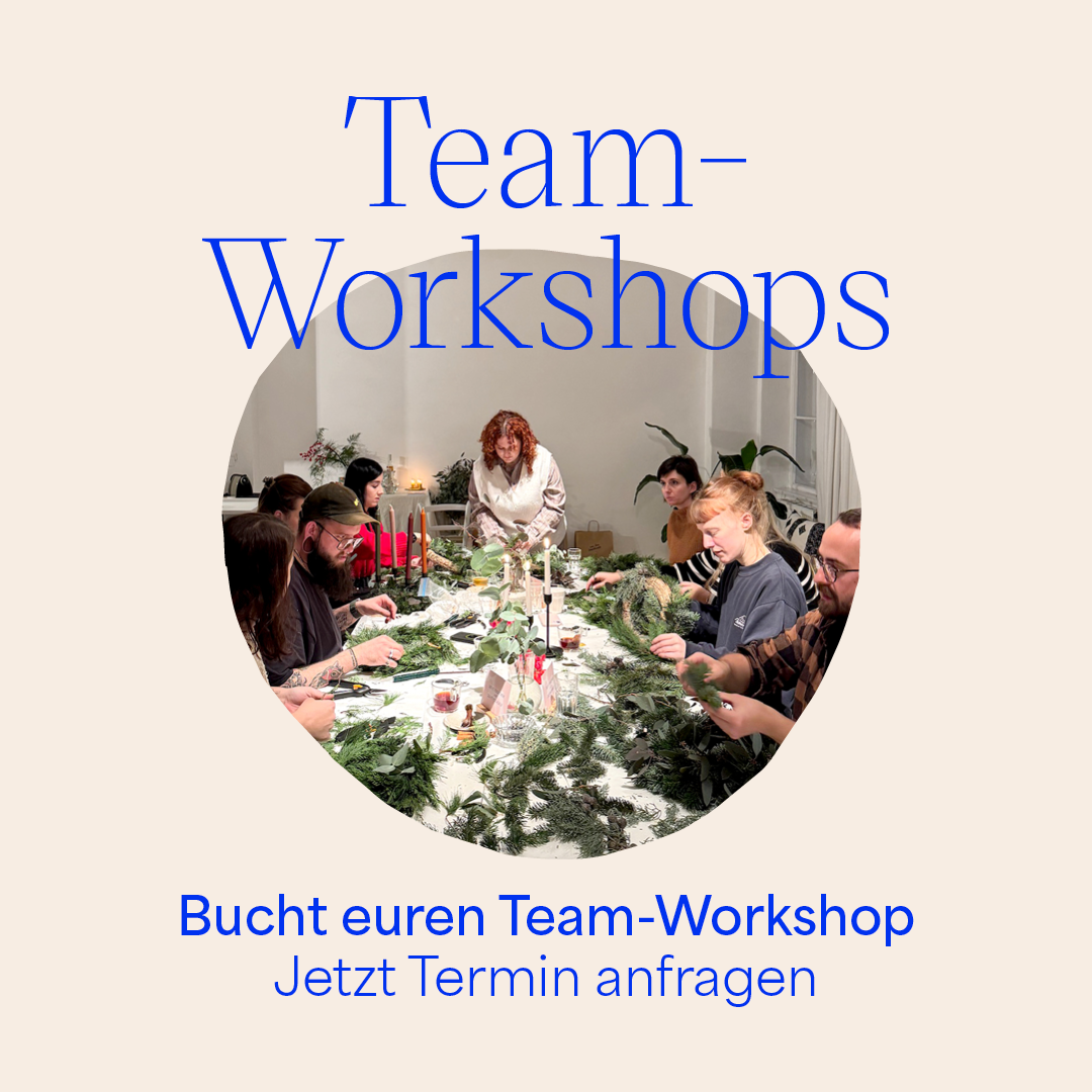 Arbeitskollegen binden gemeinsam Adventskränze bei einem kreativen Teambuilding-Workshop in Wien.