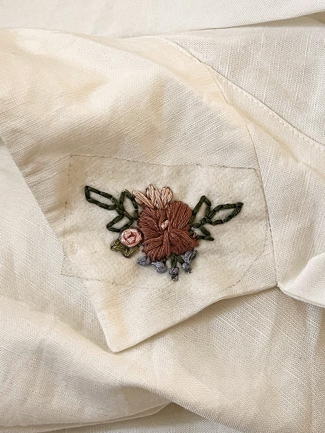 Hemdtasche mit gestickter Blüte in Altrosa und Braun mit grünen Blättern, das Stickvlies mit der Vorlage ist noch sichtbar