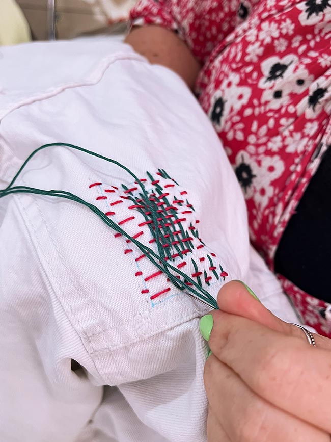 Hand mit kleinem Stickrahmen über einem Loch in heller Jeansjacke, die ersten Spannfäden für den Webstich sind gesetzt